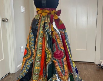 May include: A long, colorful skirt with a black top and a yellow, red, and gold patterned belt. The skirt is made of a fabric with a geometric pattern.