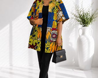 May include: A vibrant, open-front kimono-style jacket featuring a patchwork of colourful African-inspired geometric and floral patterns in shades of yellow, blue, red, and white, worn over a solid black sleeveless top and matching black trousers.