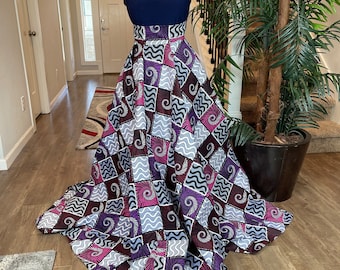 May include: A long, flowing skirt with a navy blue top. The skirt is made of a patterned fabric with a patchwork design in shades of purple, gray, and white. The skirt has a wide waistband and a full, flowing silhouette.
