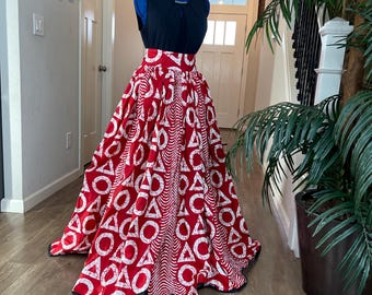 May include: A black sleeveless top and a red skirt with a white geometric design. The skirt has a full shape and a black trim. The outfit is displayed on a blue dress form. The skirt's pattern includes circles and triangles.