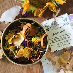 Peut inclure: Un petit bol rempli de fleurs et d'herbes séchées, y compris des pétales de rose, des pétales de tournesol et d'autres plantes. Le bol est en laiton et a une ambiance rustique et terreuse. Le texte sur l'étiquette indique "Pot-pourri artisanal naturel, Augusteaeth, Fait avec des fleurs et des herbes naturelles, chargé de magie, inspiré par le sabbat sacré de la sorcière. Merci de soutenir une petite entreprise éthique, Holdko.etsy.com".