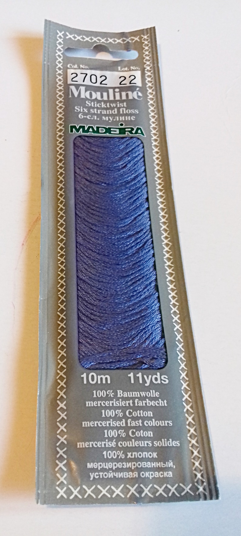 Puede incluir: Una bobina de hilo de bordar Madeira Moulin&eacute; de color morado claro. La etiqueta indica "2702 22" y especifica que el hilo es 100% algod&oacute;n, mercerizado y resistente a la decoloraci&oacute;n. La bobina contiene 10 metros (11 yardas) de hilo.