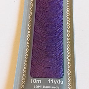 Puede incluir: Un ovillo de hilo de bordar Moulin&eacute; Madeira de color morado, etiquetado con "2710 12" y "Sticktwist Six strand floss 6-сл. мулине". El embalaje tambi&eacute;n indica "10m 11yds" y enumera el contenido de la fibra como 100% algod&oacute;n mercerizado.