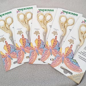 May include: Five pairs of gold embroidery scissors with a butterfly design on the packaging. The packaging is white with the text "MADEIRA" and "Gold Quality" printed on it.
