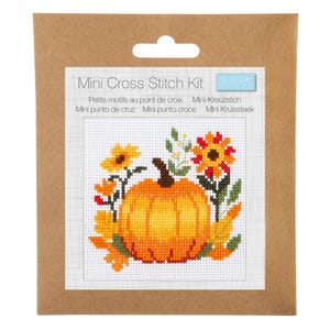 May include: A mini cross stitch kit with a pumpkin and floral design. The kit is packaged in a brown cardboard backing and includes the text "Mini Cross Stitch Kit" and text in multiple languages. The cross stitch design features a pumpkin, sunflowers, and leaves.