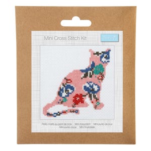 May include: A mini cross stitch kit in brown packaging featuring a pink cat silhouette filled with blue, red, and green floral patterns. The white fabric background has a grid texture, and the text reads Mini Cross Stitch Kit and Trimits.