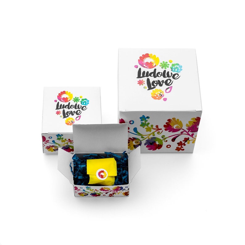 May include: Three white gift boxes with colorful floral designs and the text "Ludowe Love" on the top. The smallest box is open and contains a yellow gift bag with a blue and white floral design.