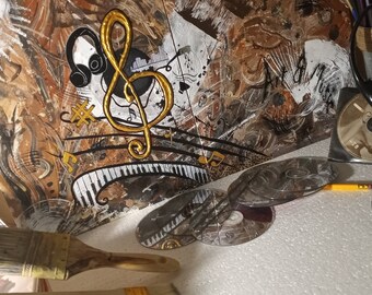 May include: A close-up of a canvas painting with a gold treble clef and musical notes. The painting is on a table with a paintbrush, CDs, and headphones.