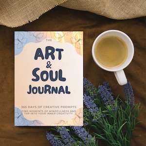 Könnte beinhalten: Ein rosa und blaues Journal mit dem Titel "The Art & Soul Journal" und dem Text "365 Days of Creative Prompts Find Moments of Mindfulness and Tap Into Your Inner Creativity."