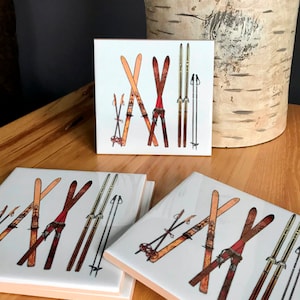 May include: Four white ceramic coasters with a vintage ski design. Each coaster features a pair of wooden skis with poles, in shades of brown, red, and gold.