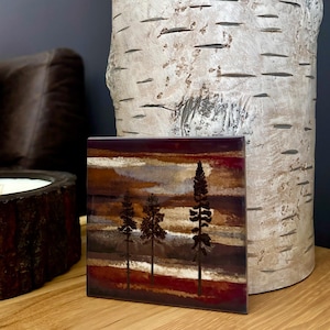 May include: Square ceramic tile with a colorful abstract design featuring a sunset scene with three trees in silhouette. The tile has a brown, red, and orange color scheme.