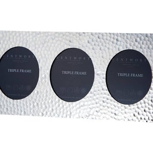 Puede incluir: Marco de fotos triple plateado con textura martillada. Cada marco tiene una abertura circular y el texto "Wentworth Design" y "Triple Frame" impreso en la parte delantera.