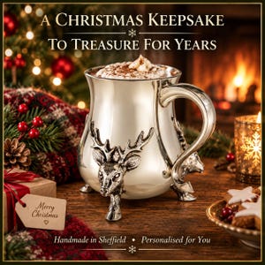 May include: A silver-toned metal mug featuring a raised deer head design and three feet, filled with a hot beverage topped with whipped cream. The text reads A CHRISTMAS KEEPSAKE TO TREASURE FOR YEARS, Merry Christmas, and Handmade in Sheffield.