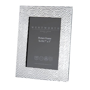 May include: A silver picture frame with a hammered texture. The frame is made by Wentworth Pewter and is designed to fit a 7 inch by 5 inch photo. The frame has the text "Wentworth Pewter" and "Picture Frame To Fit 7" x 5" printed on it.