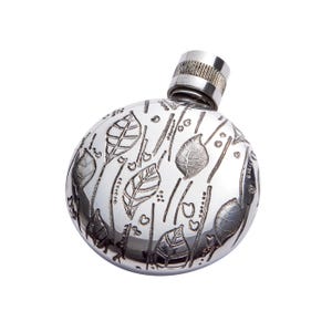 Puede incluir: Una petaca de plata con un diseño grabado de hojas y líneas. La petaca tiene un cuerpo redondo y una tapa de rosca.