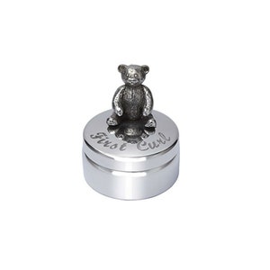 May include: A silver-coloured keepsake box with a small teddy bear figurine on top. The lid is engraved with the words "First Curl". The box is round and has a polished finish.