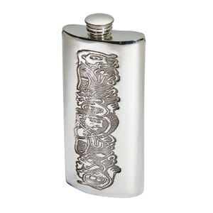 May include: A silver-coloured metal flask with a curved rectangular shape and a screw-top cap. The front surface features a vertical, deeply etched design depicting a series of stylised human figures intertwined with intricate, flowing knotwork patterns.