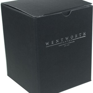 May include: A square black cardboard box with a textured finish. The front of the box features silver foil text that reads WENTWORTH PEWTER SHEFFIELD ENGLAND EST. 1946. The box has a top flap closure and is presented against a plain white background.