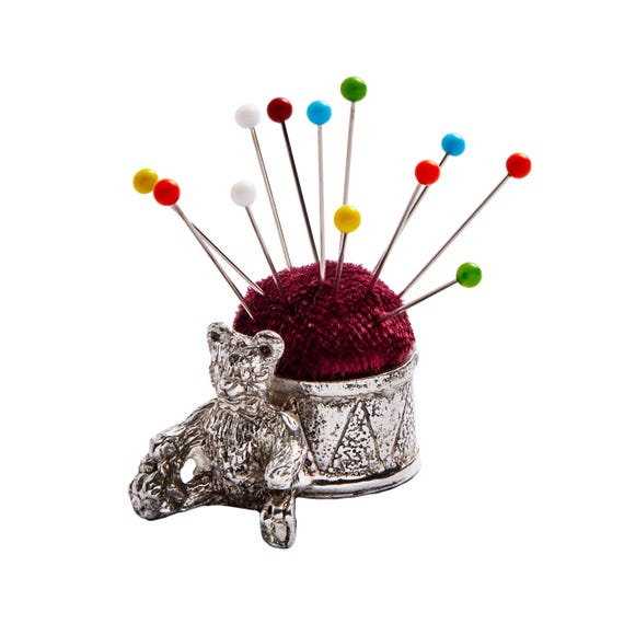 A tiny pewter teddy bear-and-drum pincushion hand-cast in Sheffield, UK — the kind of heirloom-quality sewing novelty that feels like it belongs in a Victorian curiosity shop.