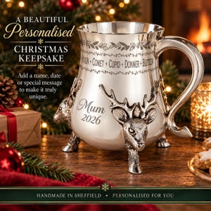 May include: A silver-toned metal mug featuring three-dimensional reindeer head accents at the base. The mug is engraved with the text Vixen, Comet, Cupid, Donner, Blitzen, Mum, and 2026. It has a curved handle and a polished finish with decorative borders.