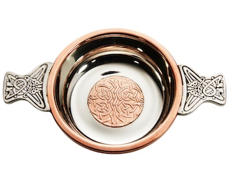 May include: A silver and copper Celtic knot design on a traditional Irish drinking cup with two handles.