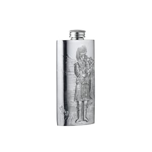 May include: A rectangular silver-coloured metal flask featuring an embossed design of a person in traditional highland attire playing bagpipes. The scene includes a mountainous landscape in the background and a screw-top cap at the top centre.