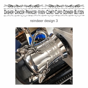 May include: A polished silver-toned metal mug featuring two sculpted reindeer heads attached to the exterior. The mug is engraved with the text DANCER PRANCER and a decorative leaf pattern. It is mounted on a machine with a visible ruler.