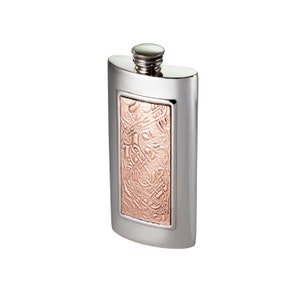 May include: A rectangular silver-toned metal flask featuring a central vertical panel with a raised copper-coloured relief of intricate, interwoven knotwork patterns. The flask has a smooth, polished finish and a small, threaded screw-top cap.