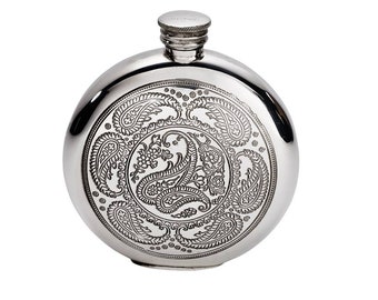May include: A round, silver-colored metal flask featuring a polished finish and a central circular panel engraved with intricate paisley patterns and floral motifs. The flask includes a small, threaded screw-top cap with a textured edge.