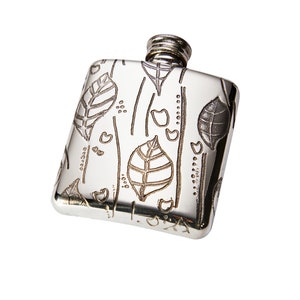 Puede incluir: Una petaca de plata con un diseño grabado de hojas y corazones.