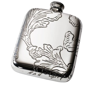 Könnte beinhalten: Ein rechteckiger Flachmann aus silberfarbenem Metall mit einem eingravierten Blumenmuster auf der Vorderseite. Der Flachmann hat eine glatte, reflektierende Oberfläche und einen kleinen, zylindrischen Schraubverschluss oben in der Mitte.