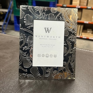 May include: Silver-plated photo frame with an ornate design featuring a repeating pattern of feathers. The frame is made by Wentworth Sheffield England and is designed to fit a 5x3 1/2 inch photograph.
