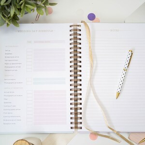 Może przedstawiać: Planer ślubny ze złotą spiralą i białym długopisem w czarne kropki. Planer ma r&oacute;żowo-niebiesko-ż&oacute;łty gradient z napisem "Wedding Day Schedule" u g&oacute;ry.