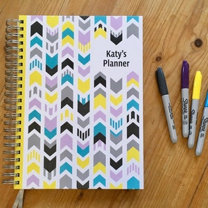 Personalised Teacher planner with different colour arrows going in opposite directions on the cover,  Silver wire and Ribbon.