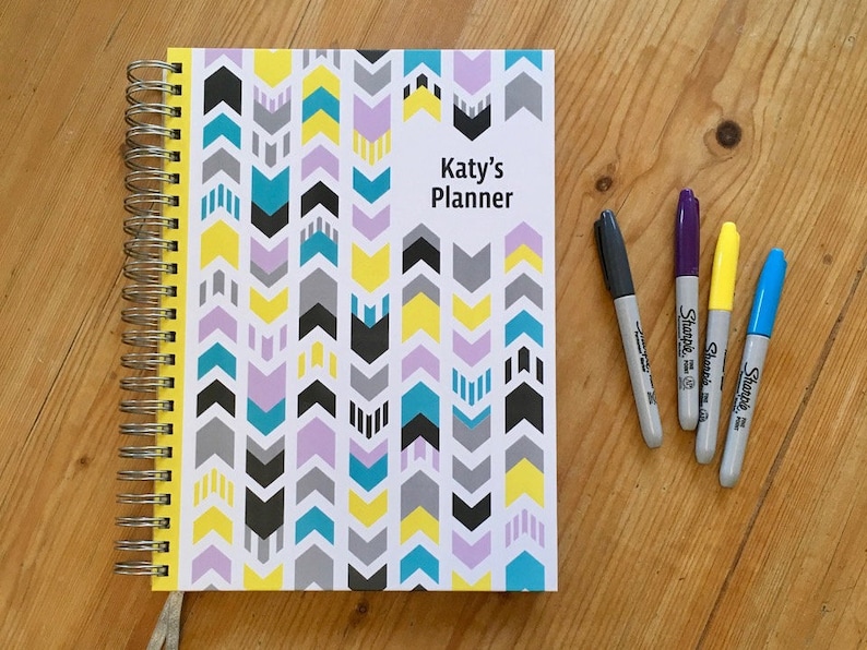 Personalised Teacher planner with different colour arrows going in opposite directions on the cover,  Silver wire and Ribbon.