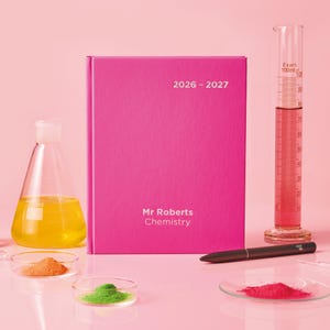 May include: A pink 2026-2027 chemistry notebook with the text "Mr Roberts Chemistry" is surrounded by lab equipment, including a flask with yellow liquid, a graduated cylinder, and petri dishes with colored powders. A black pen rests nearby.