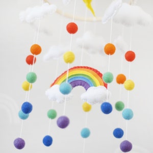 May include: A rainbow-colored felt mobile with clouds and colorful pom-poms hanging from a wooden ring.