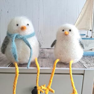 May include: Two white felt bird ornaments with yellow pipe cleaner legs. One bird is wearing a blue scarf.