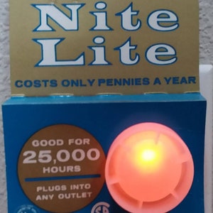 May include: A white plastic night light with a red glow, plugged into an electrical outlet. The packaging says "Crest Nite Lite" and "Good for 25,000 hours".