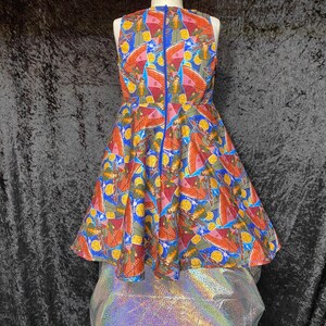 May include: A sleeveless, knee-length dress with a vibrant, patterned design. The dress features a blue zipper down the back and a full skirt. The pattern includes figures, wings, and yellow circles on a blue, orange, and red background.