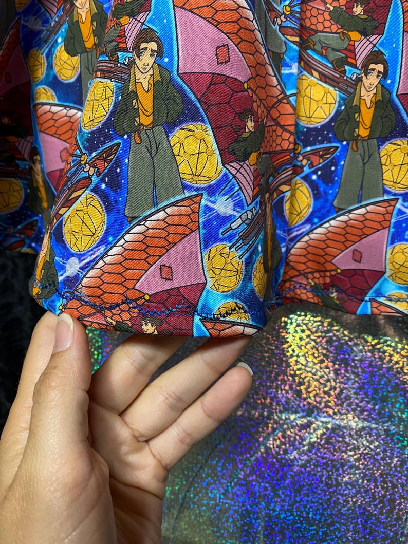May include: A colorful fabric featuring a repeating pattern of a cartoon character in a green jacket and yellow shirt, set against a blue starry background. The design includes orange and pink airships and yellow geometric shapes.