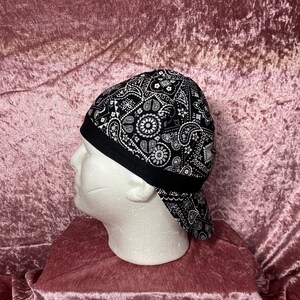 May include: Black and white bandana-style hat with a paisley pattern. The hat has a black brim and a black band around the crown.