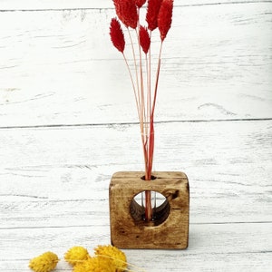 May include: A rustic wooden vase with a round opening and a glass test tube insert. The vase is stained a dark brown colour and has a natural wood grain. The vase is filled with dried red flowers.