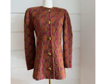 May include: A long-sleeved jacket featuring a textured brown, orange, and magenta geometric pattern. The garment has a round neckline, structured shoulders, and a front closure secured by five circular gold-toned metal buttons.