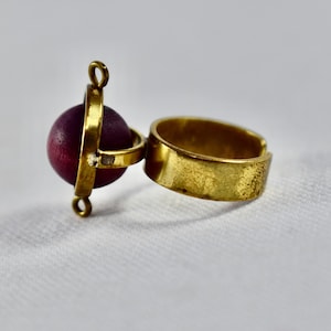 May include: A gold ring with a spinning purple wooden sphere attached. The ring is open and has a textured finish.