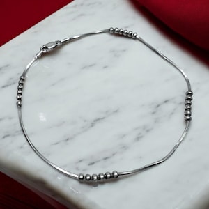 May include: A silver chain anklet with small round beads. The anklet has a clasp closure.