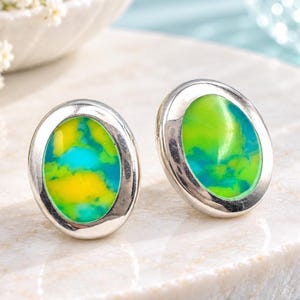 May include: A pair of oval stud earrings featuring polished silver-tone metal settings. Each earring contains a smooth, rounded inlay with a vibrant, marbled pattern of bright yellow, lime green, and turquoise blue colors.