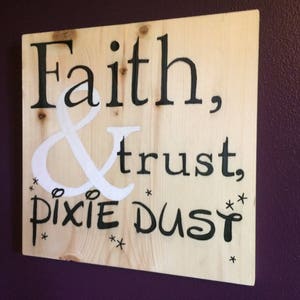 May include: A wooden sign with the text "Faith, & trust, pixie dust" in black lettering. The ampersand is white and there are small stars around the text.