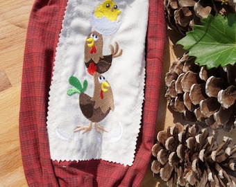 Puede incluir: Una bolsa de tela roja con un diseño bordado de tres pollos de dibujos animados. Los pollos son marrones con crestas rojas y plumas verdes. Un pollito amarillo sale de un huevo en la parte superior.