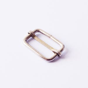 May include: A silver metal buckle with a rectangular shape and a smooth finish.